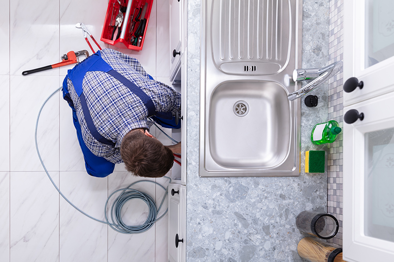 Plumber Cleaning Clogged Sink Pipe Young Male Plumber Cleaning Clogged Sink Pipe In Kitchen